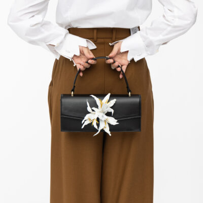 Klassische Lederhandtasche in schwarz mit weißer Lilie hinter Rücken von Model gehalten