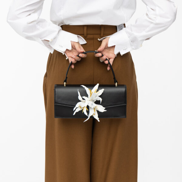 Klassische Lederhandtasche in schwarz mit weißer Lilie hinter Rücken von Model gehalten