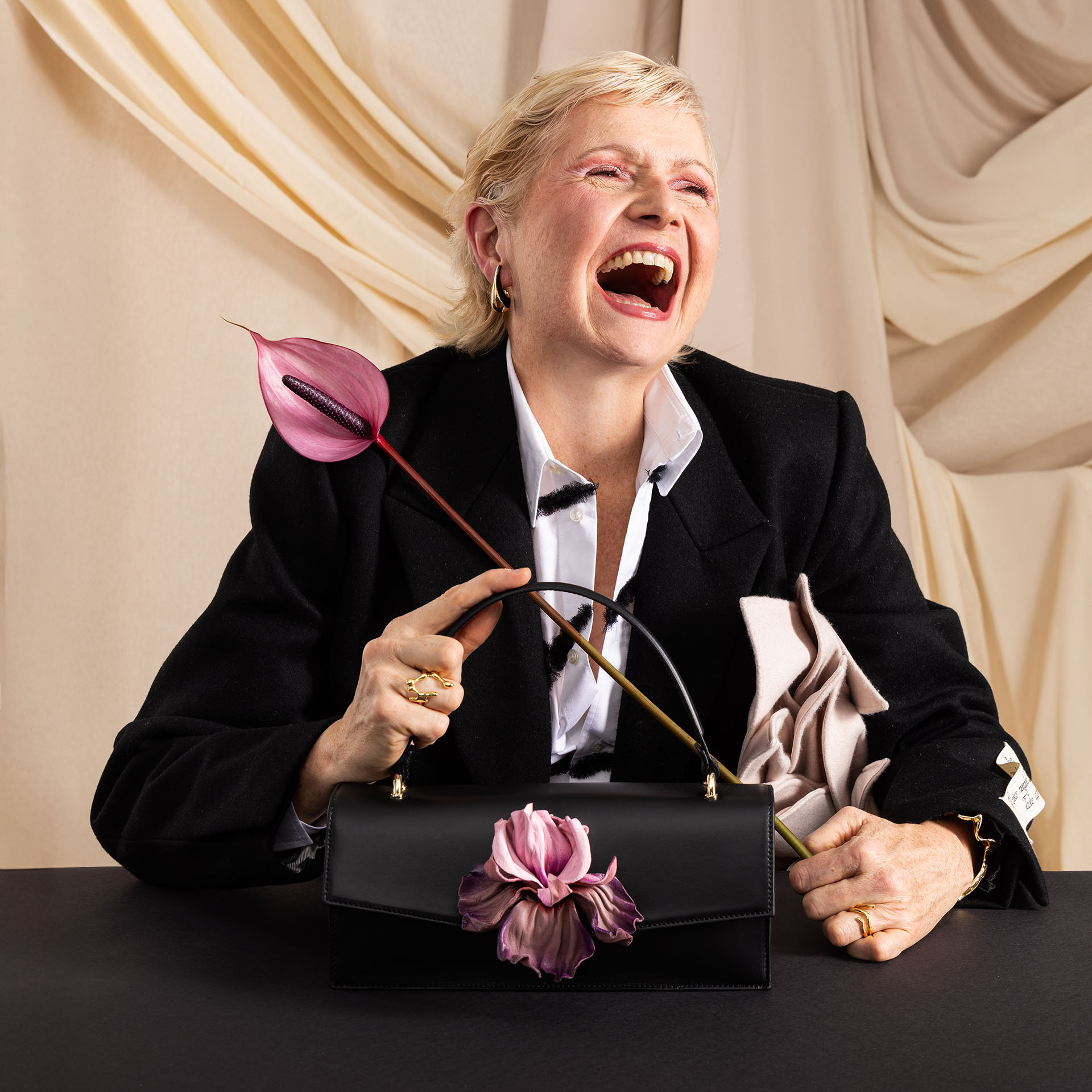 Klassische Handtasche aus schwarzem Leder mit Blume Iris und lachendem älterem Model am Tisch sitzend