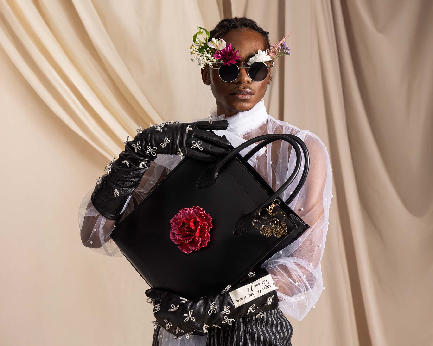 Shopper aus Leder in schwarz mit pinker austauschbarer Pfingstrose, getragen von POC-Model mit bestickten Handschuhen