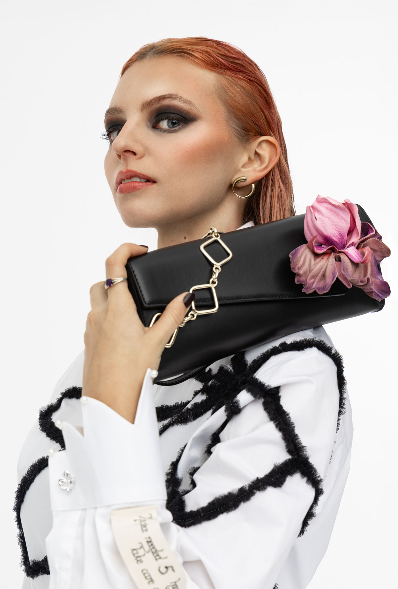 Clutch aus schwarzem Leder Modell "Posy" mit goldener Tragekette und Irisblume, gehalten von Model