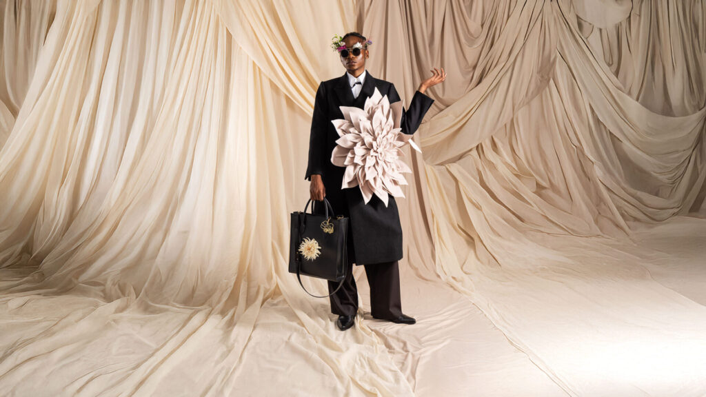 exklusive Shopper-Handtasche in schwarz mit Dahlienblüte, getragen von Model in schwarzem Mantel mit großer Blumenapplikation in Studio 