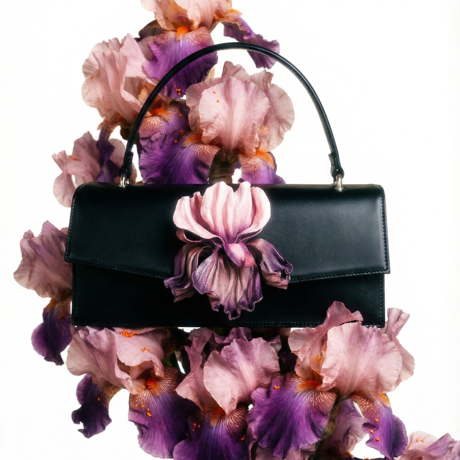 Lederhandtasche klassisch aus schwarzem Leder mit Irisblume aus Leder auf der Vorderseite, in Arrangement aus rosa Irisblumen