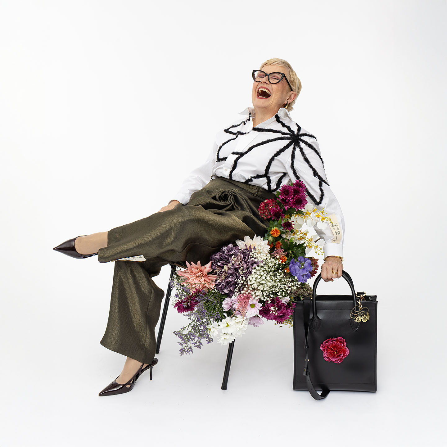 Ledershopper Modell 'Bouquet' in Schwarz mit abnehmbarer pinker Pfingstrose, neben lachendem Model sitzend