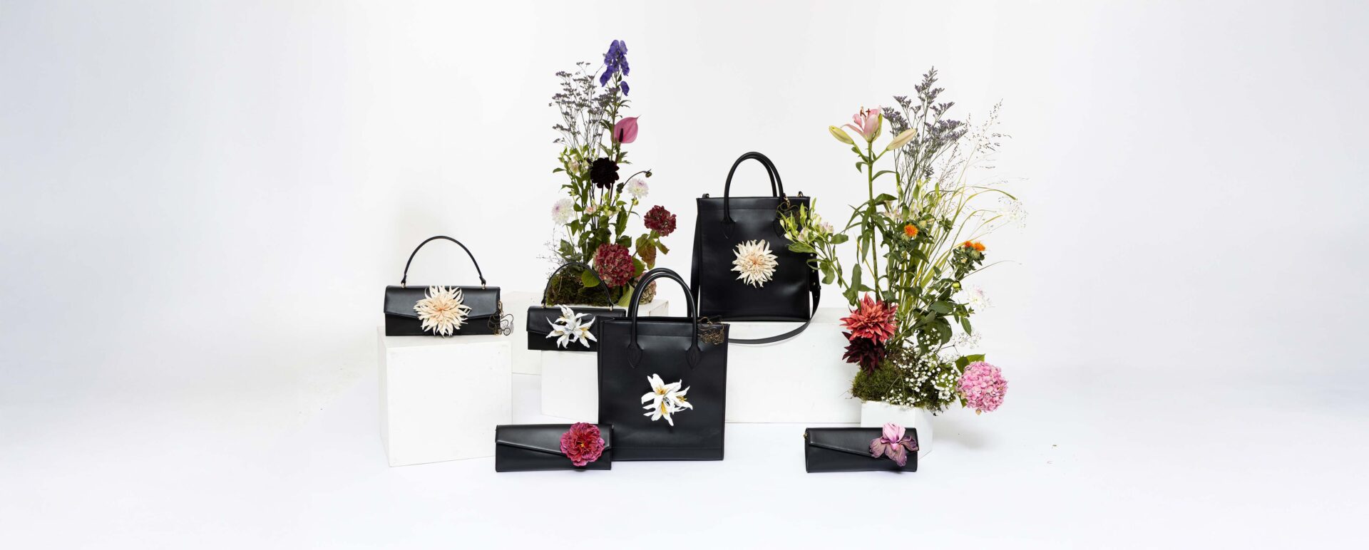 Premium Lederhandtaschen als Stilleben arrangiert auf Sockeln in weißem Studio mit Blumendetails 