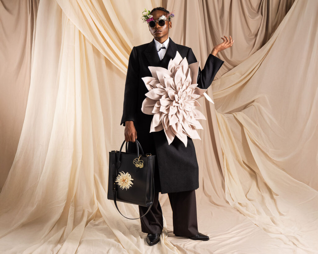 Shopper aus Leder in schwarz mit weißer, abnehmbarer Dahlienblüte, getragen von Model in Mantel mit Blumenapplikation